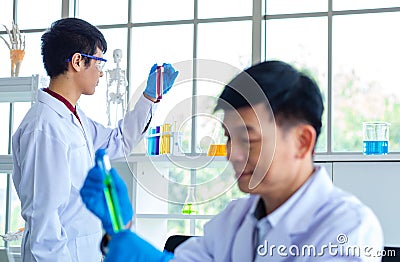 Portrait shot of Asian professional mature male scientist in white lab coat and rubber gloves sitting look at camera smiling Stock Photo