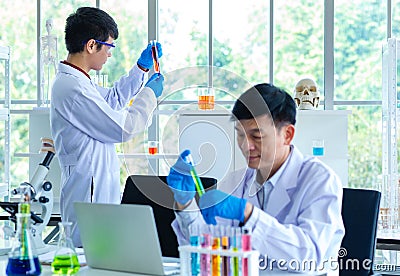 Portrait shot of Asian professional mature male scientist in white lab coat and rubber gloves sitting look at camera smiling Stock Photo