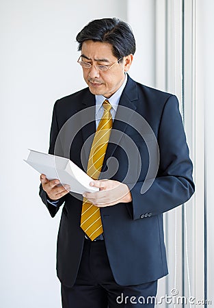 Portrait shot of Asian senior old successful wise businessman in formal suit with brown necktie and golden eyeglasses standing Stock Photo