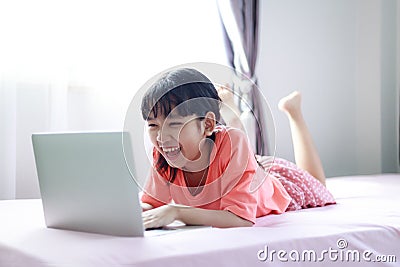 Portrait shot little Asian girl using a laptop computer to learn from home and laying on the bed with happiness, self-quarantine Stock Photo