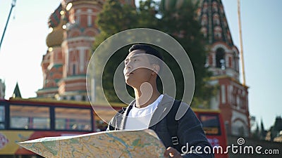 Portrait shot of a young Asian man looking at map. The Cathedral of Vasily the Blessed on background, Moscow Russia. Red Stock Photo