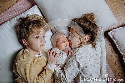 Portrait of siblings cuddling newborn, little baby. Girl lying with her new sibling in bed, closed eyes. Sisterly love Stock Photo