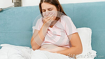 Portrait of sick pregnant woman feeling nausesa and coughing while lying in bed at morning. Healthcare and intoxication Stock Photo