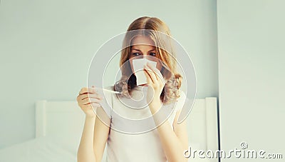 Portrait of sick upset woman sneezing blow nose using tissue and measuring checking body temperature looking at thermometer on the Stock Photo