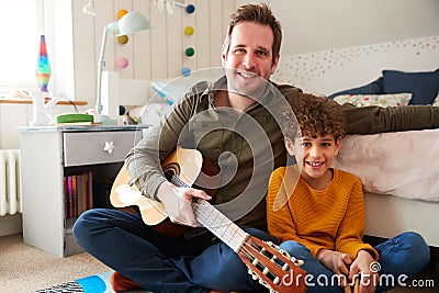 Portrait Of Single Father At Home With Son Playing Acoustic Guitar In Bedroom Stock Photo