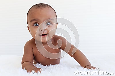 Portrait of a six month crawling African American baby on fluffy white rug, happy smiling adorable sweet little girl kid lying on Stock Photo