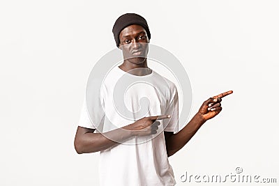 Portrait of skeptical and judgemental african-american guy in beanie, pointing fingers right and grimacing disappointed Stock Photo