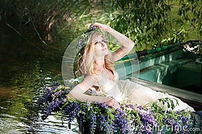 Portrait of slavic or baltic woman with wreath sitting in boat with flowers. Summer Stock Photo