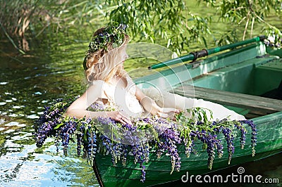 Portrait of slavic or baltic woman with wreath sitting in boat with flowers. Summer Stock Photo