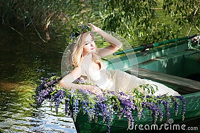 Portrait of slavic or baltic woman with wreath sitting in boat with flowers. Summer Stock Photo