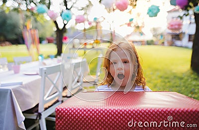 Portrait of small girl with large present box outdoors in garden in summer. Stock Photo