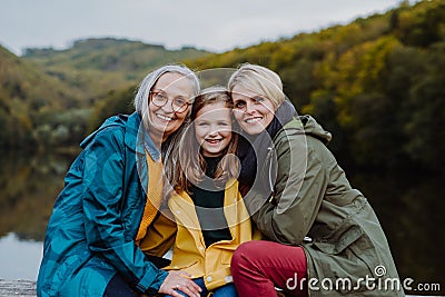 Portrait of small girl with mother and grandmother sitting and looking at camera outoors in nature. Stock Photo