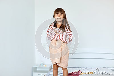 Portrait of small girl wearing large striped shirt and beige short pretending to be a grown up woman. Girl child posing in Stock Photo