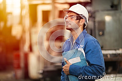 Portrait of smart engineer education machine service manual book happy worker standing proudly in heavy industry background Stock Photo