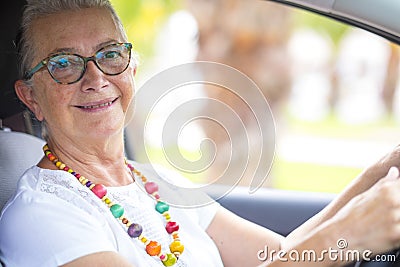 Portrait of a smiling attractive senior woman with eyeglasses enjoying drive her car. Travel and transportation concept Stock Photo