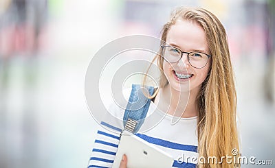 Portrait of a smiling beautiful teenage girl with dental braces. Young schoolgirl with school bag and tablet device Stock Photo