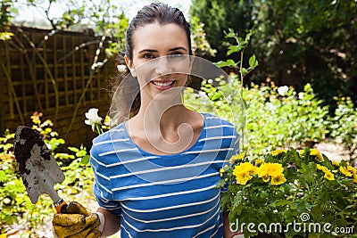 Portrait of smiling beautiful woman holding trowel and flowering pot Stock Photo