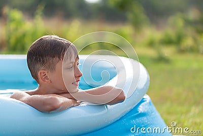 Portrait of smiling boy splashing in an inflatable pool on a sunny summer day in nature. Child staying cool in the summer heat Stock Photo