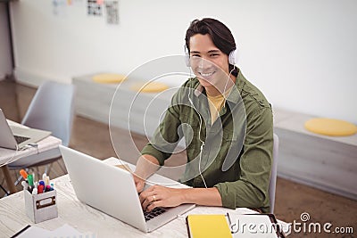 Portrait of smiling businessman working over laptop at desk while wearing headphones Stock Photo