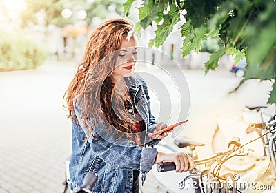 Portrait of smiling at camera red curled hair caucasian teen girl unlocking bike at Bicycle sharing point using the modern Stock Photo