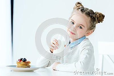 portrait of smiling child with glass of milk in hand and homemade pancakes with honey and berries Stock Photo