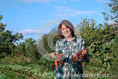 Portrait of a smiling elderly woman with a crop of carrots and lights with tops in her hands in the garden Stock Photo