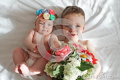 Portrait of smiling Europeans blond boy with blue eyes and girl on a white background with a bouquet of flowers. Stock Photo