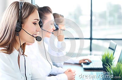 Portrait of smiling female customer service agent wearing headset with colleagues working in background at office. Stock Photo