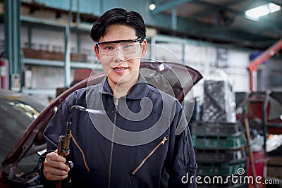 Portrait of smiling handsome Asian mechanic man in uniform welding car body panel vehicle, auto mechanic technician fixing, Stock Photo