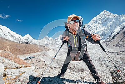 Portrait of smiling Hiker man with Nuptse 7861 m peak and Gorak shep settlement background with trekking poles, UV protecting Stock Photo