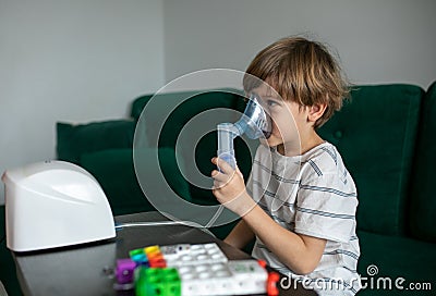 Portrait of smiling ill preteen boy making inhalation with nebulizer, holding mask vapor with hand, breathing steam. Stock Photo