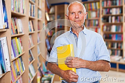 Portrait of smiling intelligent older man in library with book in hands Stock Photo