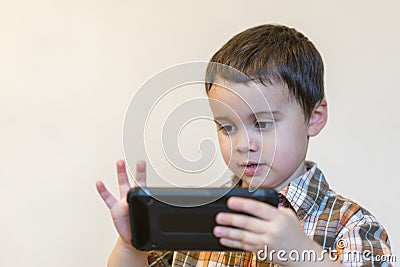 Portrait of a smiling little boy holding mobile phone over light background. cute kid playing games on smartphone Stock Photo