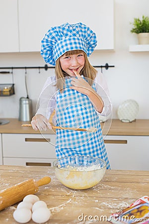 Portrait of a smiling little girl in a cook clothes tests a dough in a bowl Stock Photo