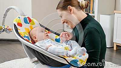 Portrait of smiling mother sitting next to baby son rocking in electric rocker. Child development and childhood Stock Photo