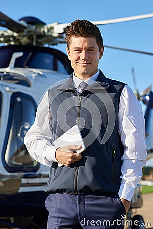 Portrait Of Smiling Pilot Standing In Front Of Helicopter With D Stock Photo