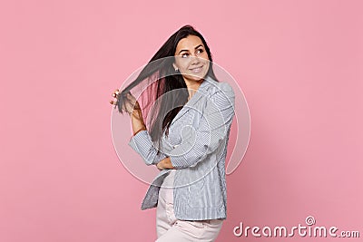 Portrait of smiling pretty thinkful young woman in striped jacket holding hair and looking aside isolated on pink pastel Stock Photo