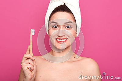 Portrait of smiling pretty woman with astonished facial expression, holds toothbrush over pink background and looking Stock Photo