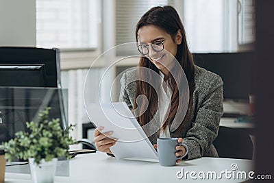 Portrait of smiling pretty young business woman in glasses sitting on workplace and working with documents Stock Photo