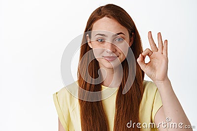 Portrait of smiling redhead woman looks confident, shows okay zero sign, no proble gesture, assure you, guarantee Stock Photo