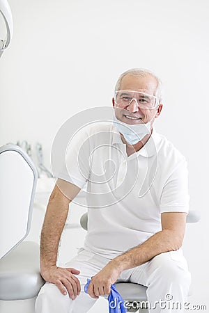 Portrait of smiling senior dentist sitting on chair at dental clinic Stock Photo