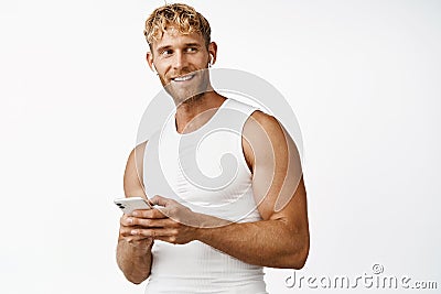 Portrait of smiling strong sportsman with mascules, holding smartphone, using sport app, standing over white background Stock Photo