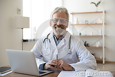 Portrait of smiling trusted middle aged old doctor at workplace. Stock Photo