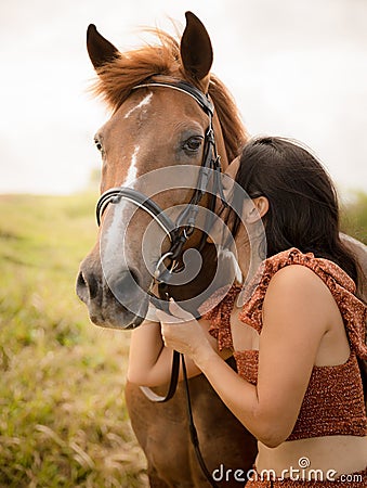 Portrait of smiling woman and brown horse. Asian woman kissing horse. Romantic concept. Positive emotions. Love to animals. Nature Stock Photo