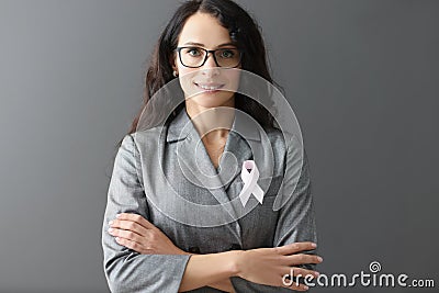 Portrait of smiling woman in gray suit on her chest with pink ribbon symbol of fight against breast cancer Stock Photo