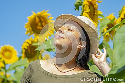 Portrait of a smiling 40-year-old woman in a straw hat against a background of blooming sunflowers. Photo shoot against the backgr Stock Photo