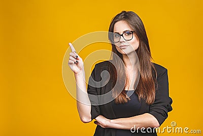 Portrait of smiling young business woman pointing up and looking at the camera isolated against yellow background Stock Photo