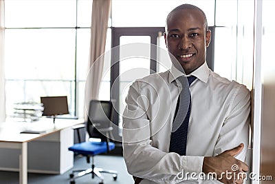 Portrait of smiling young businessman with arms crossed leaning on cupboard in office Stock Photo