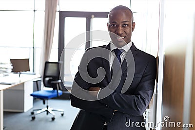 Portrait of smiling young businessman standing arms crossed leaning on cupboard in office Stock Photo