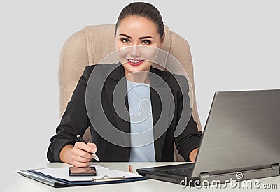 Portrait of a smiling young businesswoman wears a formal business suit working on a laptop while sitting at a table in an office Stock Photo